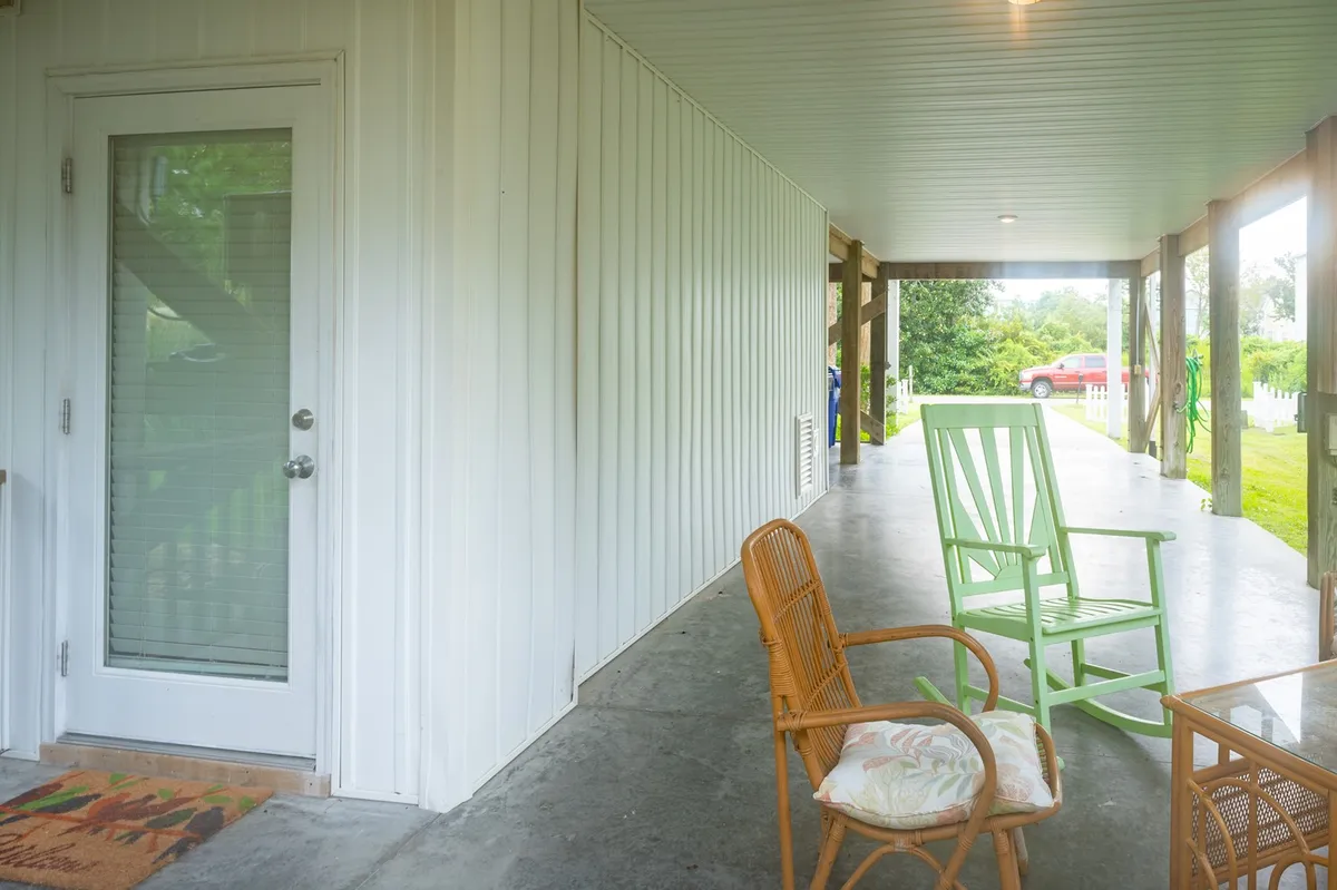 A welcoming porch space featuring a green rocking chair and a rattan chair, set beside the entry door. The area suggests a spot for enjoying the morning sun, sipping coffee, and engaging in casual conversation, with an ambiance that hints at gentle breezes and relaxation.