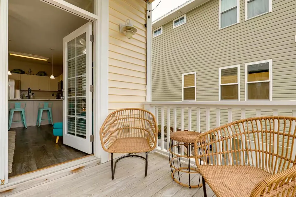 This exterior image features outdoor seating just outside a door, with a glimpse into the kitchen, suggesting fluid indoor-outdoor living. The inviting setting is ideal for group meals, oyster roasts, or unwinding after exploring the neighborhood.