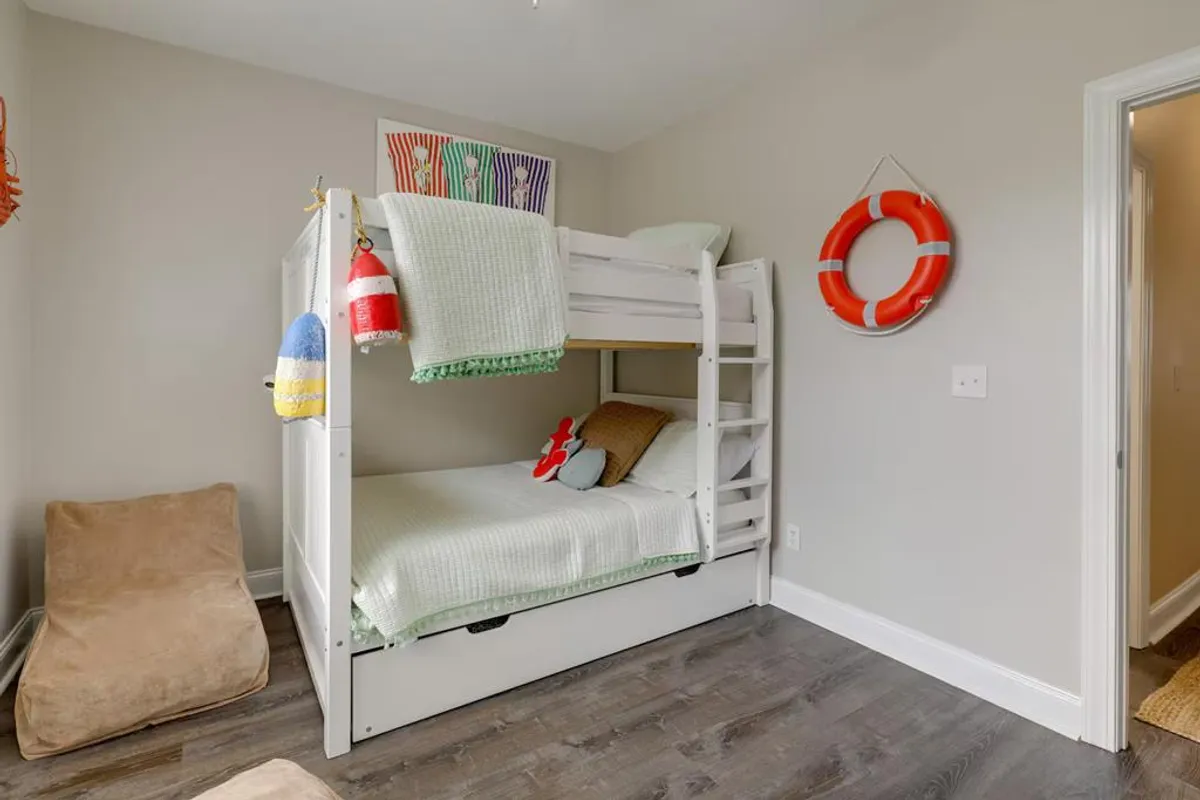 A cheerful and cozy bunk room featuring a bunk bed, bean bag chair, playful life preserver decoration, and colorful artwork. The setting suggests a fun and safe space for kids or teens to play, read, or share stories late into the night.