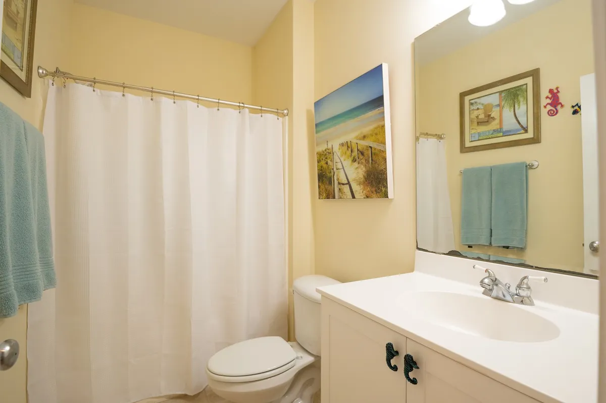 A modern bathroom with a sleek sink, shower curtain, tasteful artwork, and fluffy towels ready for guests. The calm palette provides a spa-like feel, underscoring the convenience of ensuite baths in each bedroom.