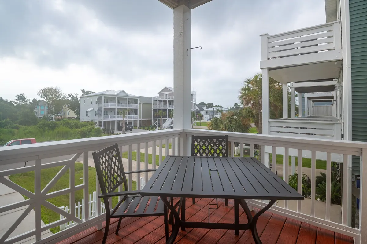 An outdoor balcony scene with a table and chairs overlooks the surrounding neighborhood. The relaxed atmosphere suggests a spot for morning coffee, evening chats, or planning group outings, with fresh air and open views reinforcing connection to the locale.