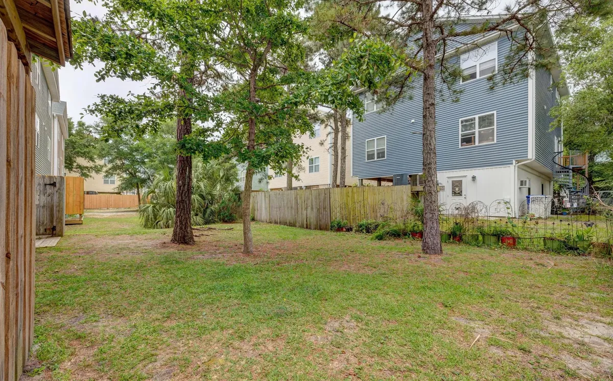 A calm, inviting backyard framed by mature trees and bordered by a fence, with neighboring houses visible beyond. The yard offers ample grassy space ideal for pets to play or for family gatherings, suggesting an environment where both relaxation and recreation are welcomed.