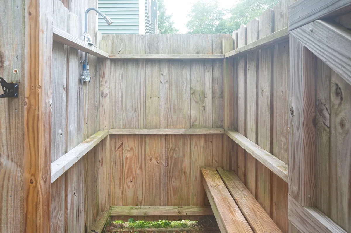 This image features a wooden outdoor shower area with a modern shower fixture, bench, and handy shelves for storing beach gear or towels. Wooden walls enhance the coastal vibe and suggest a refreshing space to rinse off after beach adventures.