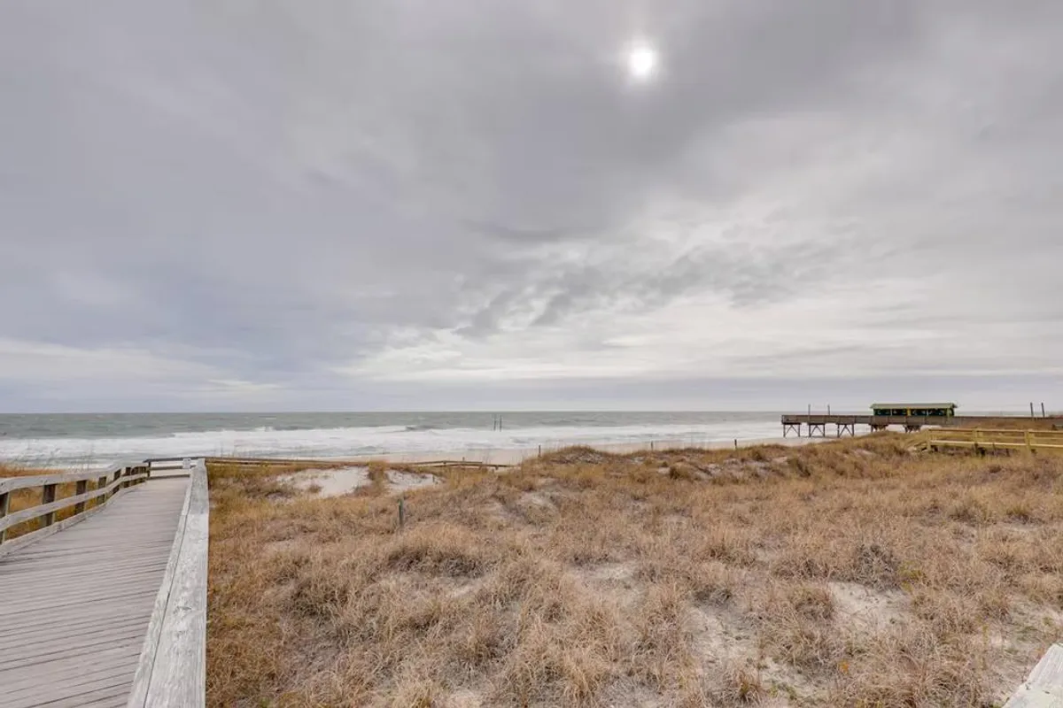 A beautiful stretch of sandy beach meeting the tranquil ocean, with a boardwalk leading toward the water. The setting invites leisurely walks and offers a sense of the broader natural environment accessible from the property.