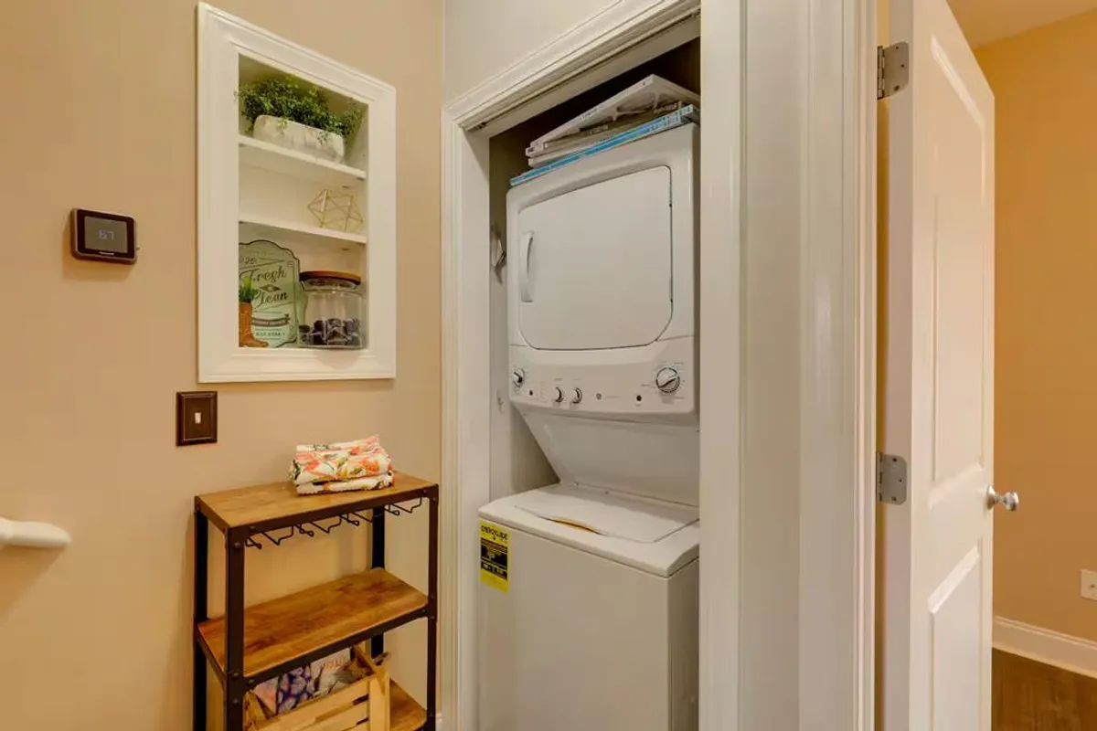 This image features a washer and dryer unit set within a tidy laundry space. There are wooden shelves for organizing laundry essentials and a decorative plant that adds a touch of hominess. The area appears clean, organized, and easily accessible, reflecting a practical amenity for guests.